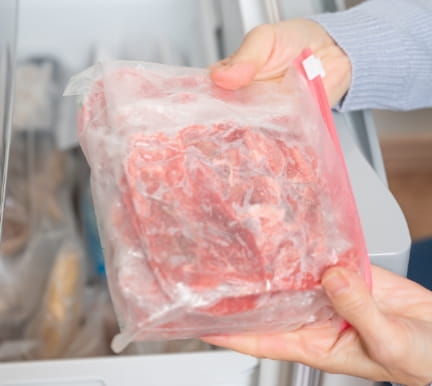冷蔵庫の中で肉の袋を持つ人物の画像