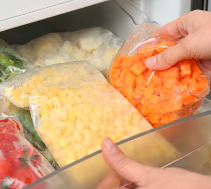 冷蔵庫を開けて野菜を袋に入れている人の画像